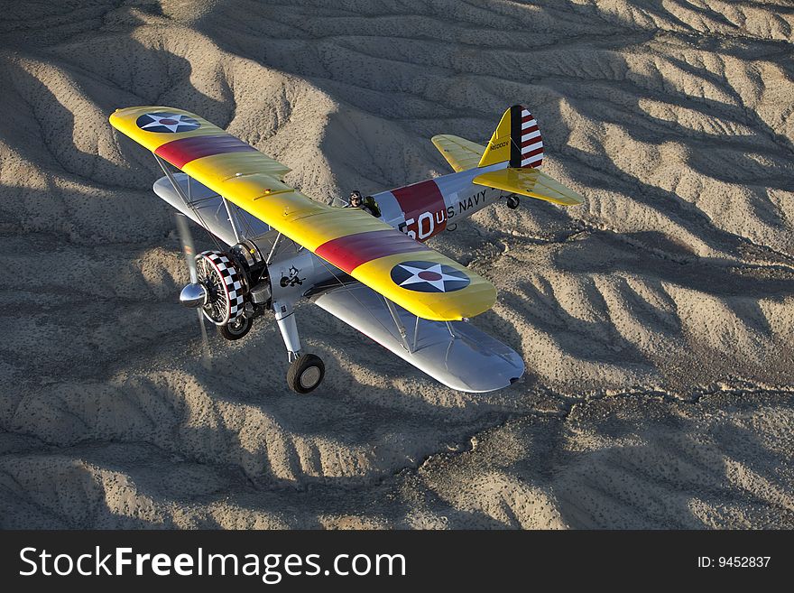 Yellow 1942 steerman flying over rugged desert. Yellow 1942 steerman flying over rugged desert