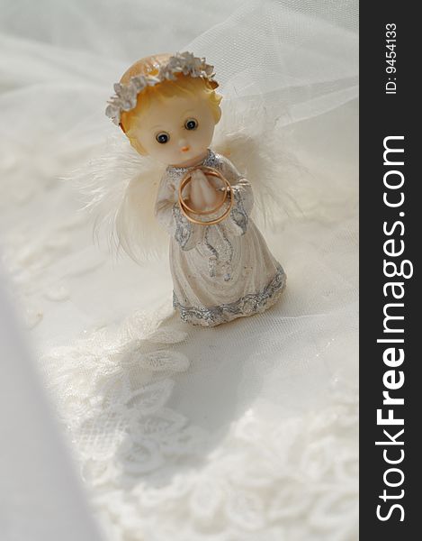 Photo of a figure of a small angel with the wedding rings, standing on a wedding fabric.