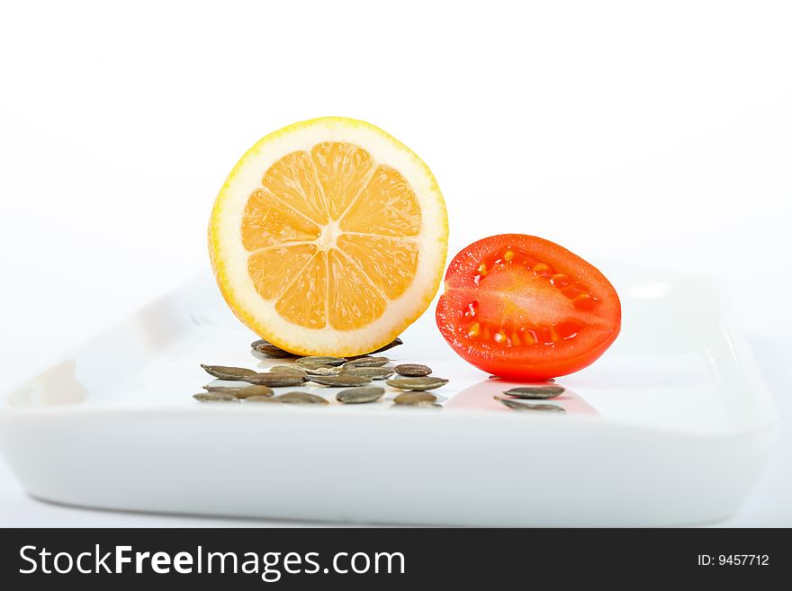 Lemon, tomato and pumpkin seeds on a white plate. Lemon, tomato and pumpkin seeds on a white plate