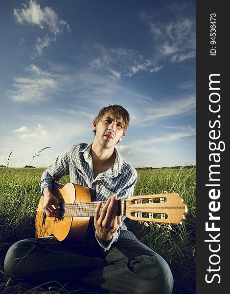A man playing an acoustic guitar on a field. A man playing an acoustic guitar on a field.