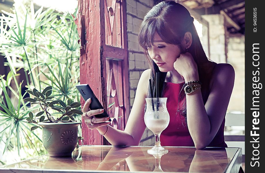 A young woman checking her phone while drinking a beverage.