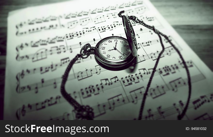 A pocket watch on top of sheet music. A pocket watch on top of sheet music.