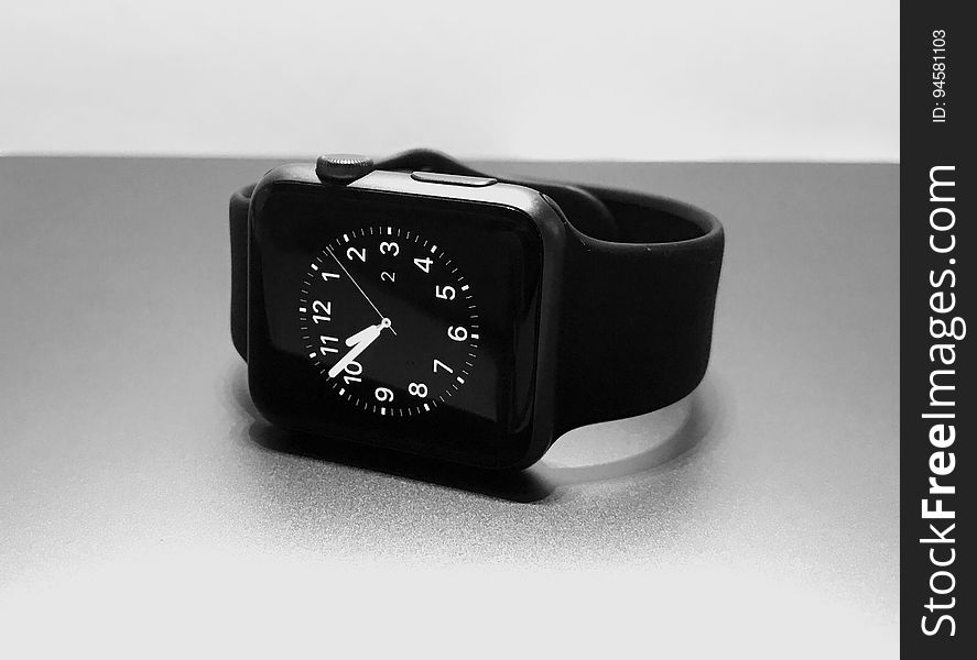 Electronic wrist watch with black strap and dial and white minute, hours and second hands lying on its side on a table. Electronic wrist watch with black strap and dial and white minute, hours and second hands lying on its side on a table.