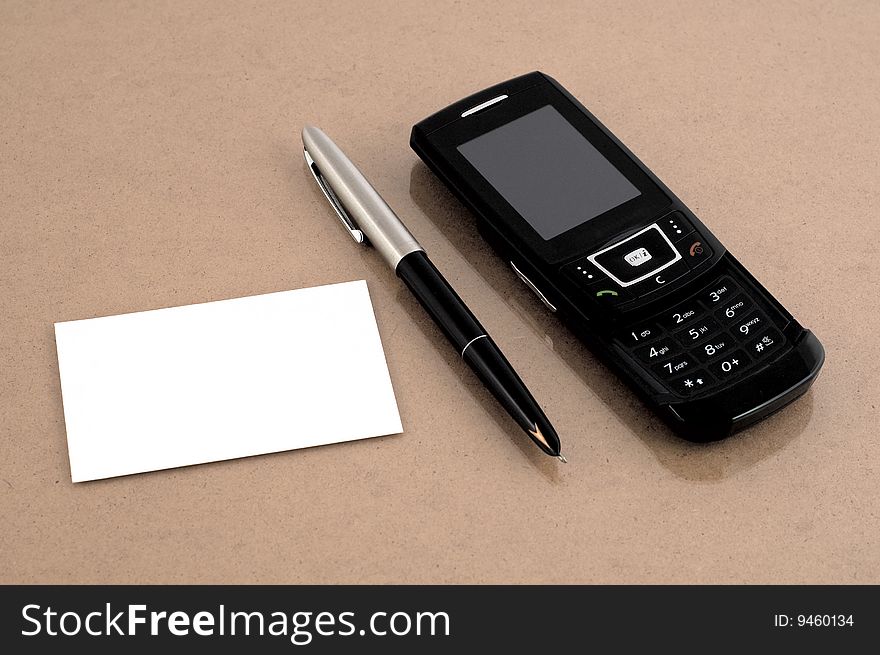 Mobile phone with pen and blank business card at brown desk