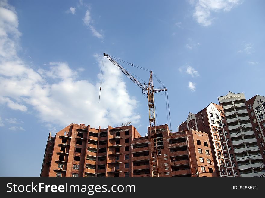 Brick house under construction, tower crane against blue sky. Brick house under construction, tower crane against blue sky