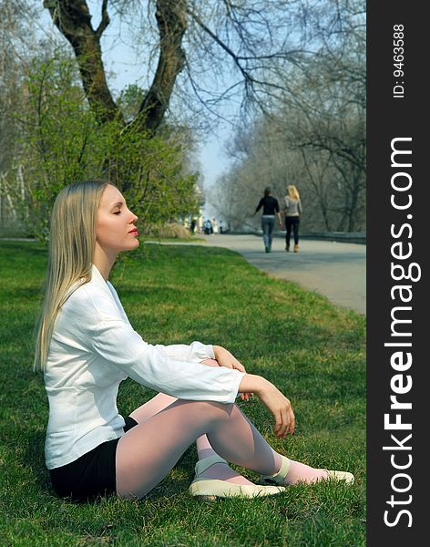 The woman sitting on a grass in park in a white blouse