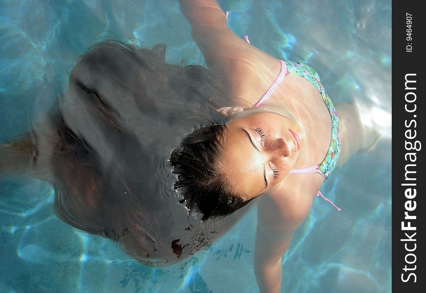 A young brown haired girl in a tropical swimming pool, floating in the water. A young brown haired girl in a tropical swimming pool, floating in the water.