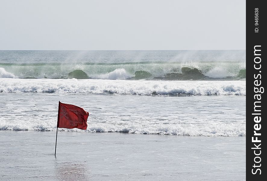 Red warning flag standing against big ocean waves. Bali, Kuta beach.