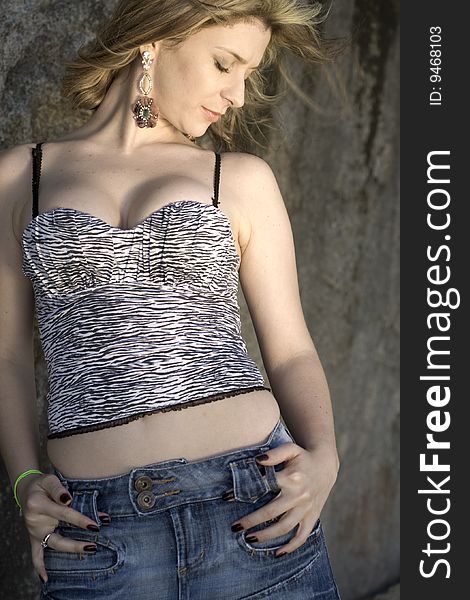 A very pretty and young blond brazilian woman wearing a black and white, zebra like top and jeans skirt next to rocks. A very pretty and young blond brazilian woman wearing a black and white, zebra like top and jeans skirt next to rocks.