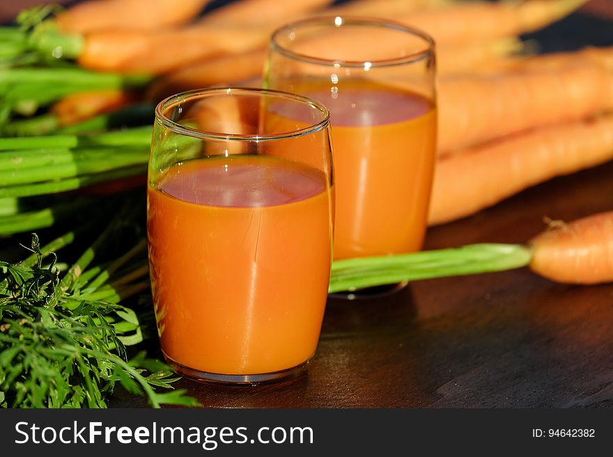 2 Clear Drinking Glass Container with Carrot Juice on Brown Wooden Tabletop in Tilt Shift Lens Photography