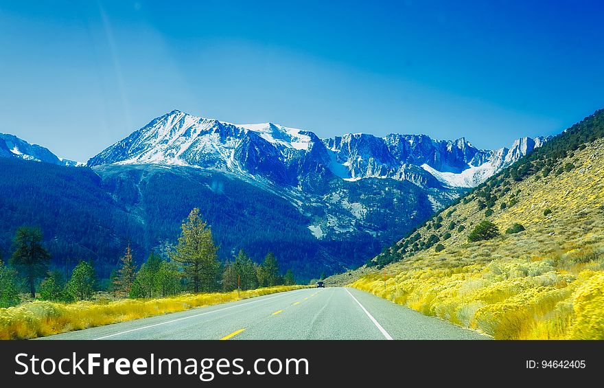 Scenic road through the snow dusted Alpine mountains with fresh green growth on both sides of road, cool blue sky. Scenic road through the snow dusted Alpine mountains with fresh green growth on both sides of road, cool blue sky.