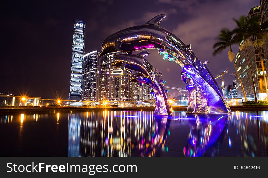 A fountain with a dolphin sculpture in a city at night. A fountain with a dolphin sculpture in a city at night.