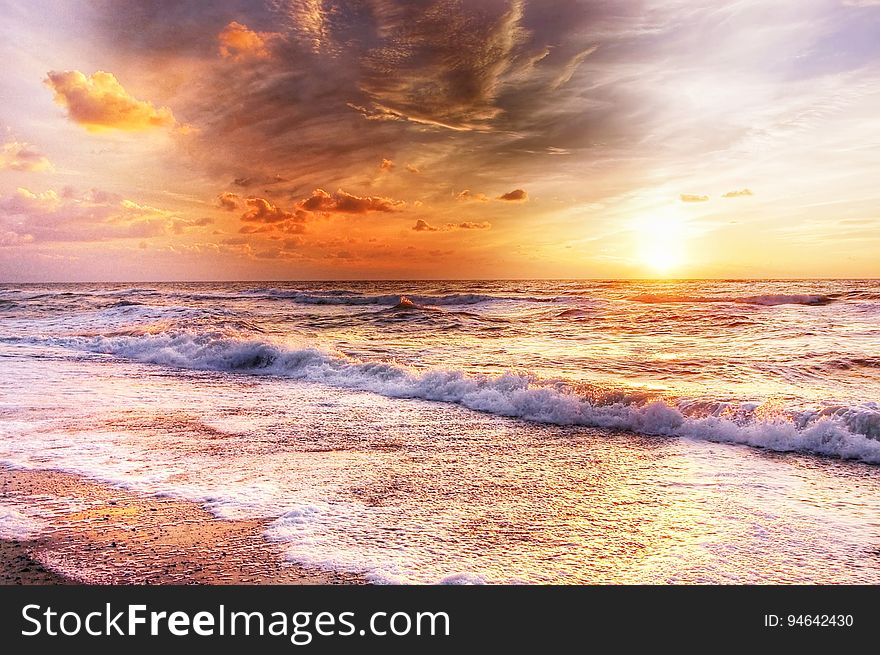 Golden sunset breaking through cloud remnants and with waves breaking onto a shingle beach. Golden sunset breaking through cloud remnants and with waves breaking onto a shingle beach.