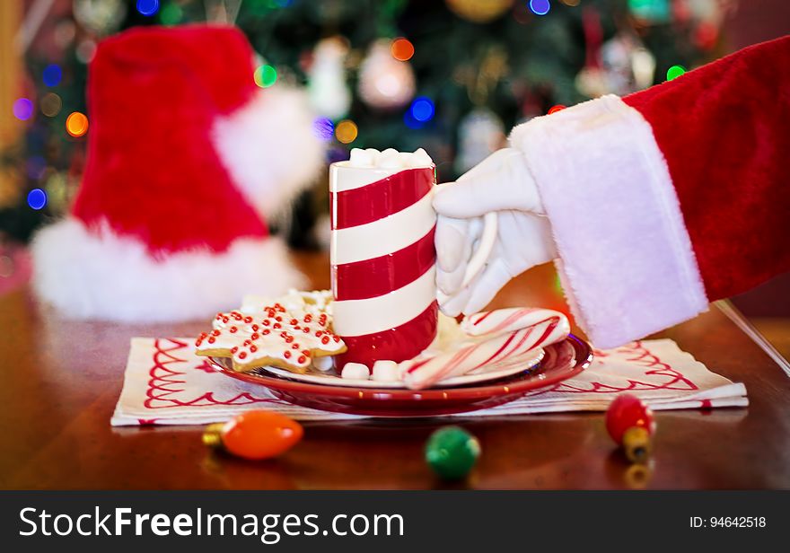 The hand of Santa Claus grabbing a cup of hot chocolate from a plate with cookies. The hand of Santa Claus grabbing a cup of hot chocolate from a plate with cookies.