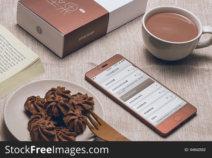 A chocolate color smartphone with a plate of chocolates and a cup of hot chocolate. A chocolate color smartphone with a plate of chocolates and a cup of hot chocolate.