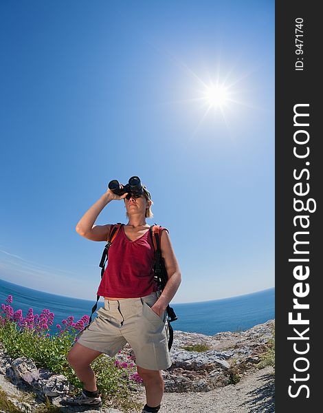 Young blonde woman hiking watching through binoculars. Copy space