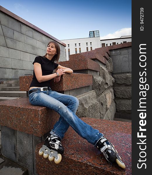 Rollerskating girl in blue jeans sitting on granite plate - wide angle portrait