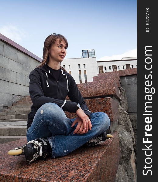 Rollerskating girl in blue jeans sitting on granite plate - wide angle portrait