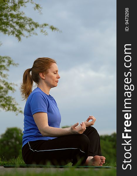 A woman sits in a lotus pose meditating with blue sky. A woman sits in a lotus pose meditating with blue sky