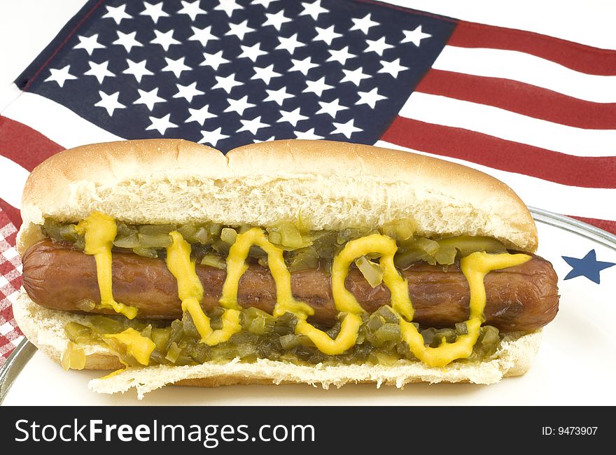 A hotdog on a plate with an American flag background, selective focus on hotdog, with shallow depth of field, horizontal with copy space. A hotdog on a plate with an American flag background, selective focus on hotdog, with shallow depth of field, horizontal with copy space