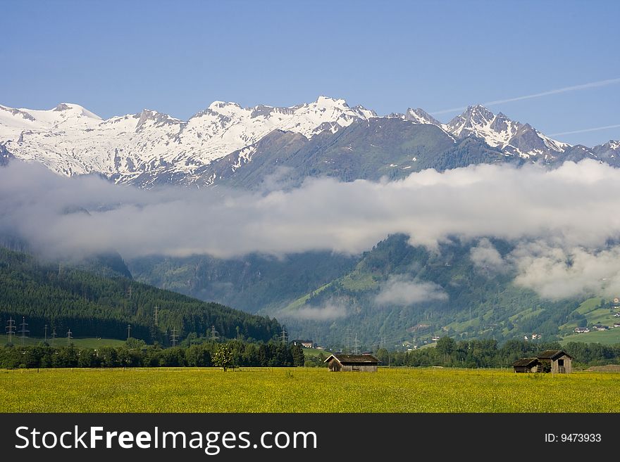 Green field with snow capped Alpine mountains in background, Zell am See, Austria. Green field with snow capped Alpine mountains in background, Zell am See, Austria.