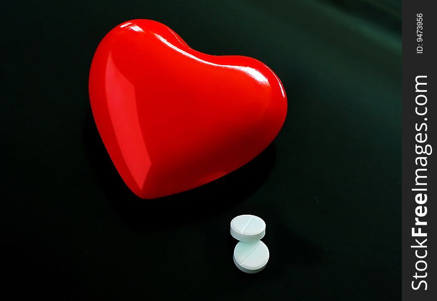 A red heart on black background lies near pills