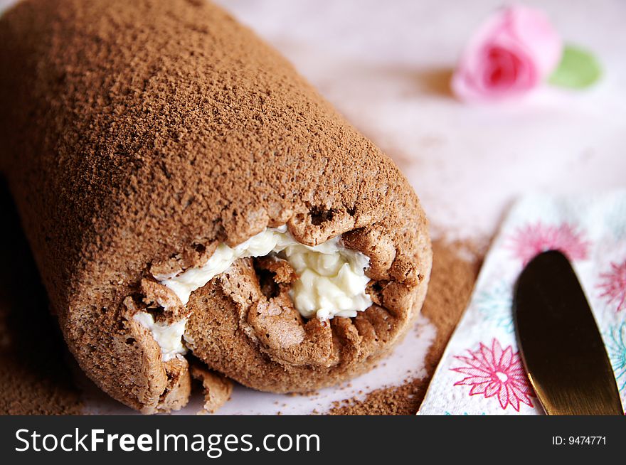 Homemade Swiss chocolate roll with vanilla butter cream dusted with cocoa, pink blur background, closeup