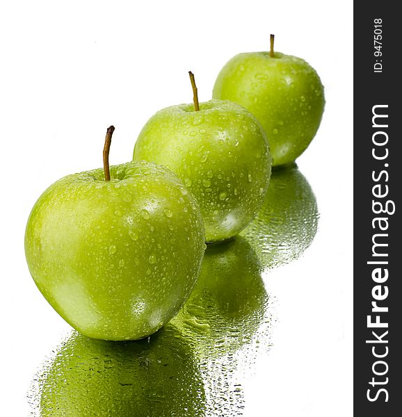 Three green apples with water drops on a mirror