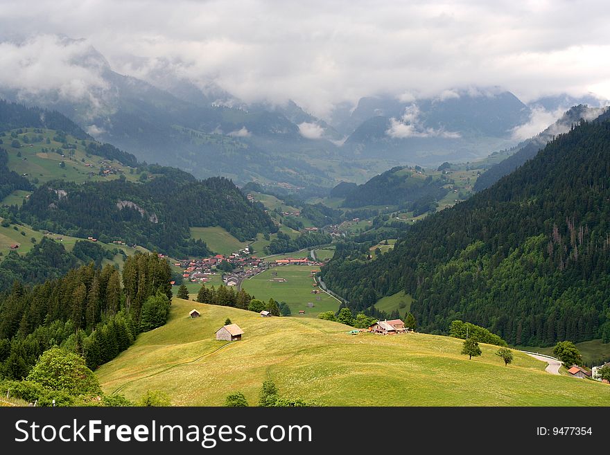 A mountain village in Switzerland, laying in a valley with could covered mountains in the background. A mountain village in Switzerland, laying in a valley with could covered mountains in the background