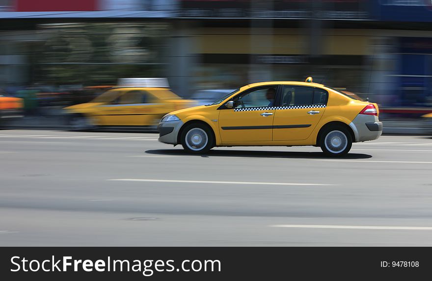 Panning image of a yellow cab in a city street.