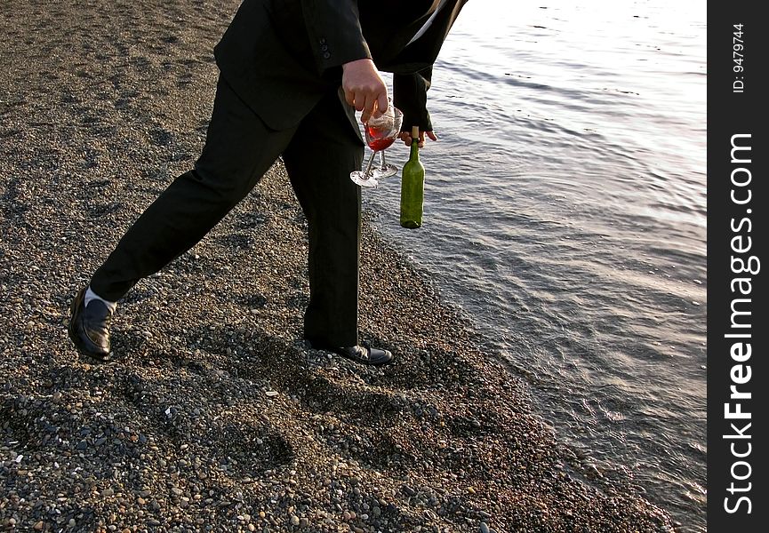 This man is falling off balance while holding two wine glasses and bottle at the beach. This man is falling off balance while holding two wine glasses and bottle at the beach.