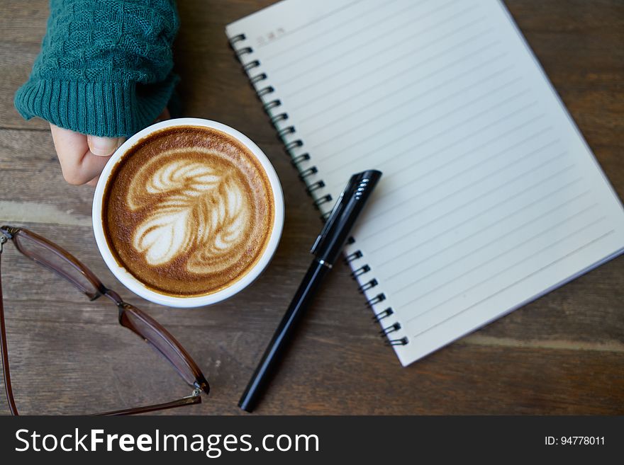 Hand holding cup of coffee next to blank open notebook and pen with eyeglasses. Hand holding cup of coffee next to blank open notebook and pen with eyeglasses.