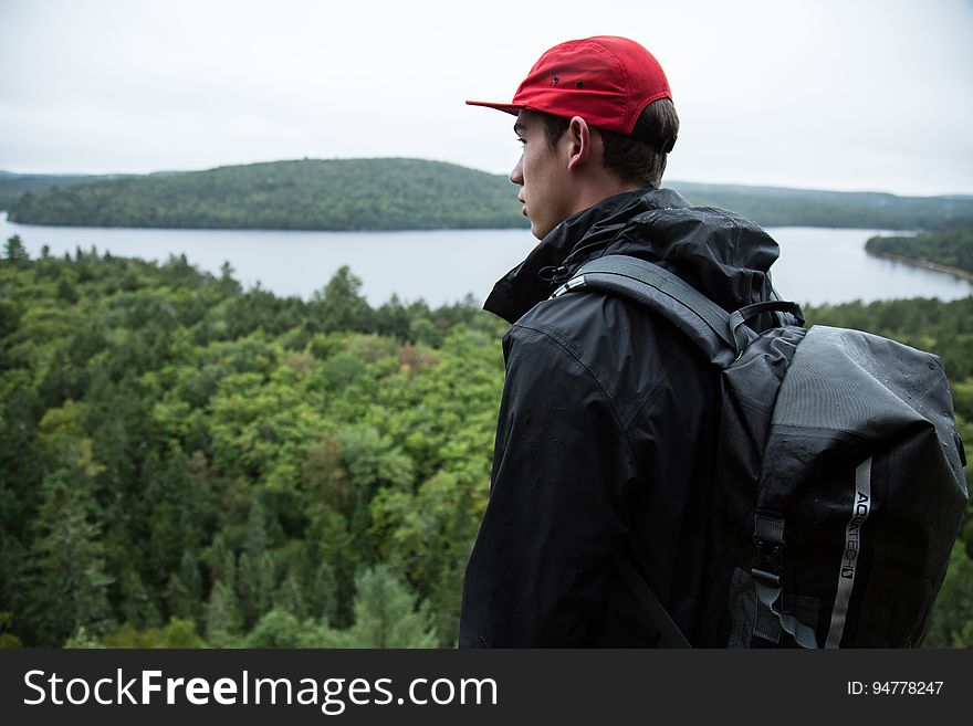 Man standing on hilltop with backpack overlooking forest along banks of lake. Man standing on hilltop with backpack overlooking forest along banks of lake.