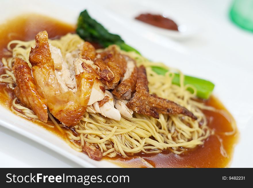 A plate of delicious chicken wing noodles, topped with mouth watering gravy sauce and complete with a tinge of vegetable stalk by the side, a delicacy in Asian countries. A plate of delicious chicken wing noodles, topped with mouth watering gravy sauce and complete with a tinge of vegetable stalk by the side, a delicacy in Asian countries.