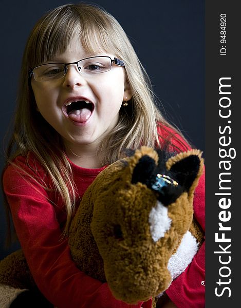 A young blonde girl playing with her soft toy horse, making a funny face, her front teeth missing. A young blonde girl playing with her soft toy horse, making a funny face, her front teeth missing.