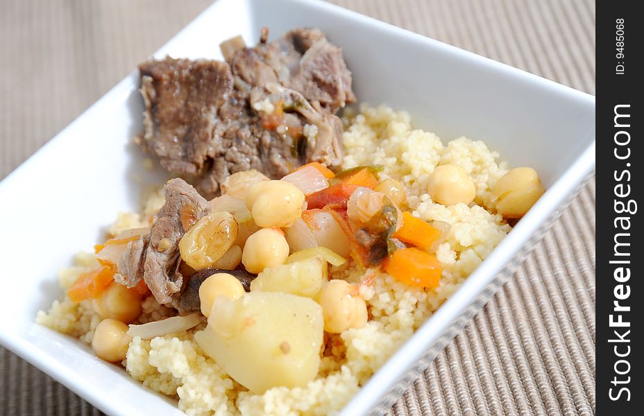 Sticky lamb with couscous, garnished with spring potatoes carrots and chickpeas