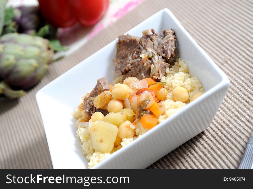 Sticky lamb with couscous, garnished with spring potatoes carrots and chickpeas