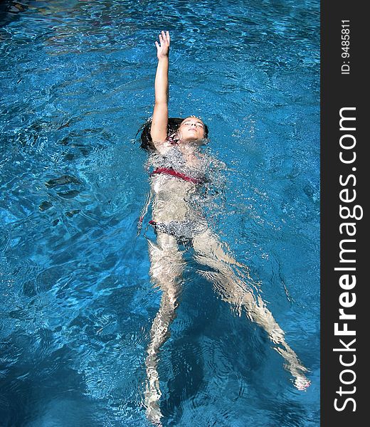 A girl in a bikini swimming the backstroke in a tropical pool. A girl in a bikini swimming the backstroke in a tropical pool.