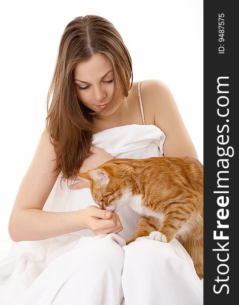 The beautiful young woman sits in bed and plays with a red cat. The beautiful young woman sits in bed and plays with a red cat