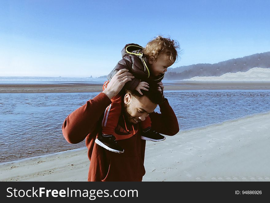 A man carrying his child over his shoulders on a beach. A man carrying his child over his shoulders on a beach.