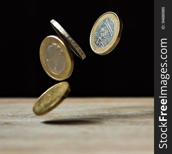Four Euro coins falling midair onto wooden table.