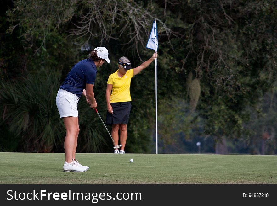 A golfer tries to get her ball into the hole while her partner looks on. A golfer tries to get her ball into the hole while her partner looks on.