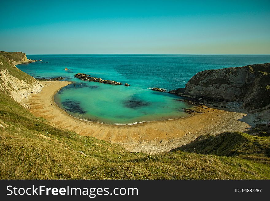 Sheltered beach on the sunny shore of an aquamarine sea with blue cloudless sky. Sheltered beach on the sunny shore of an aquamarine sea with blue cloudless sky.