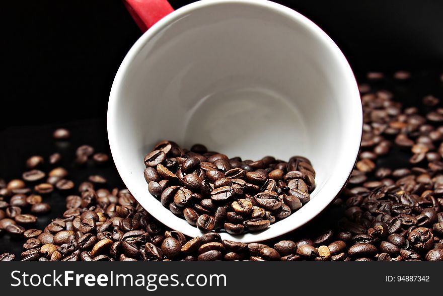 Coffee beans in and surrounding a coffee cup.