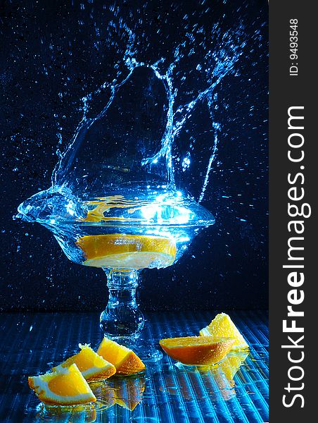 Color Photo freezing motion as orange slices are dropped in to a glass of water. Color Photo freezing motion as orange slices are dropped in to a glass of water.