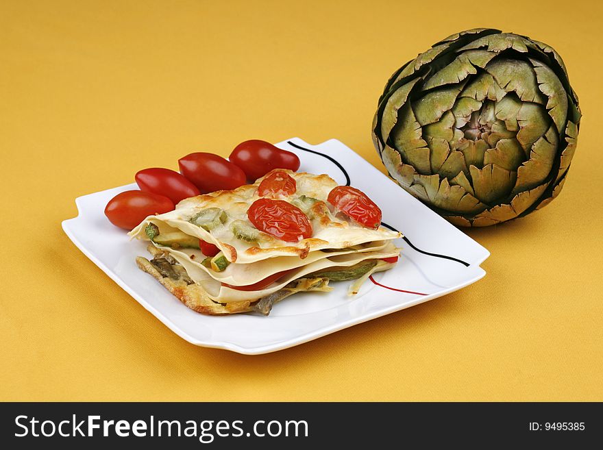 Vegetable lasagna on a yellow cloth with an artichoke. Vegetable lasagna on a yellow cloth with an artichoke