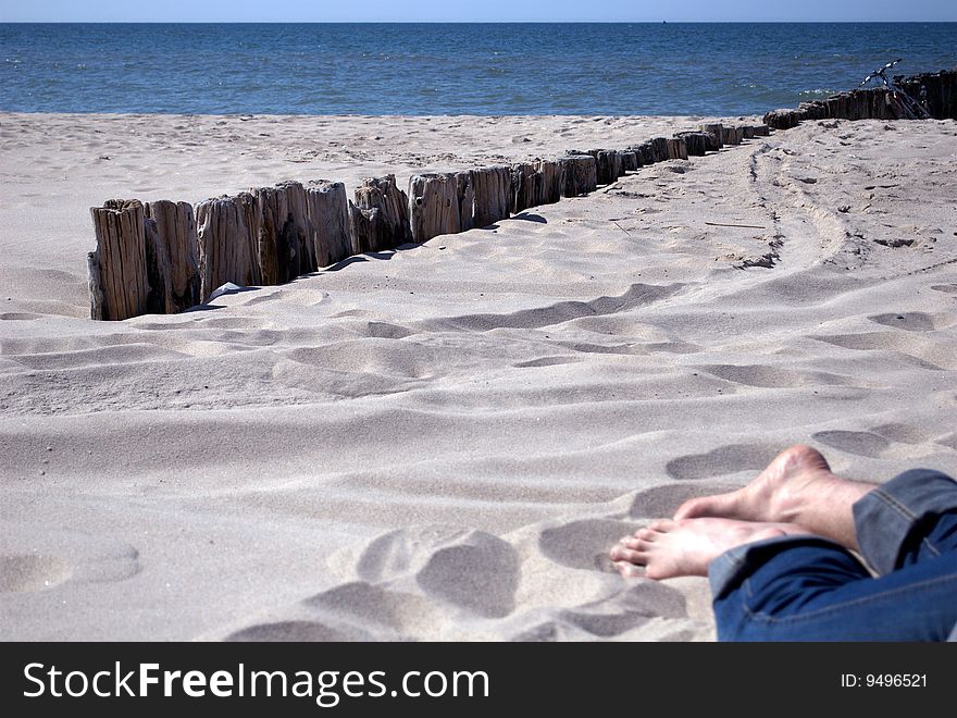 Man's feet on a sunny beach, near wooden breakwater, at the baltic sea. Man's feet on a sunny beach, near wooden breakwater, at the baltic sea
