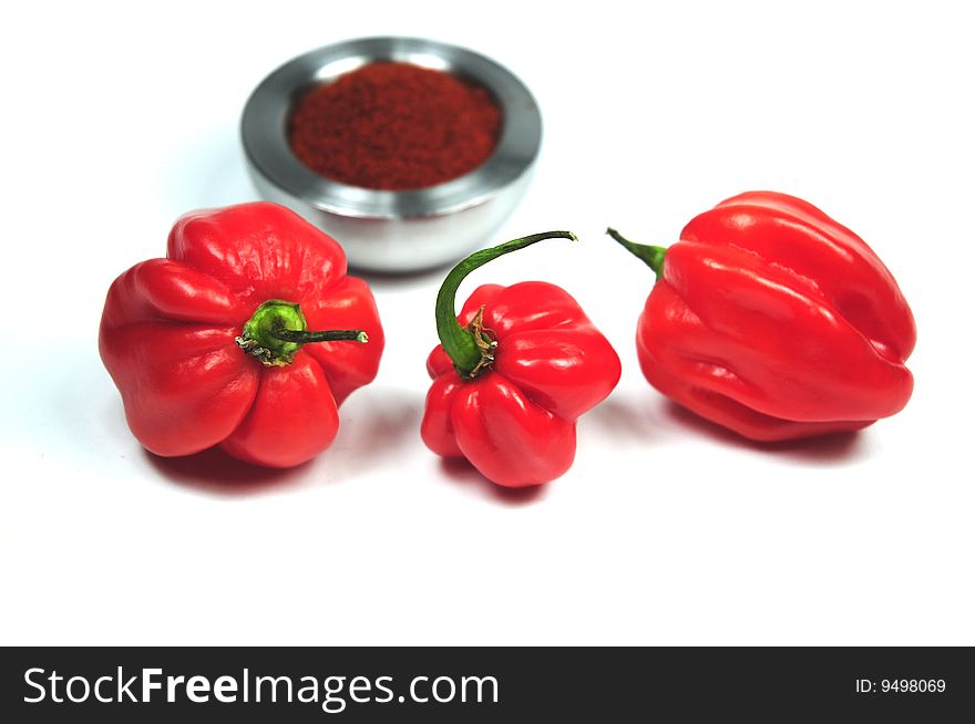 A couple of red peppers in front of a dish with dried pepper. A couple of red peppers in front of a dish with dried pepper.