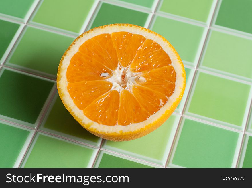 Half of the juicy orange on green tiled bar