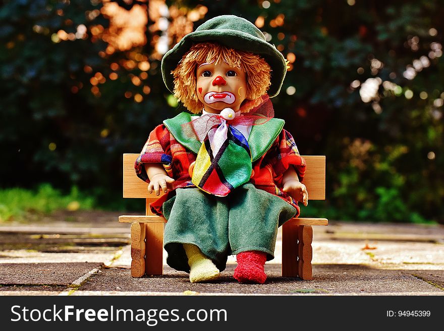 Clown doll with sad expression on wooden bench outdoors. Clown doll with sad expression on wooden bench outdoors.